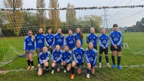 Concord Rangers U14 girls team. They are wearing a blue football kit and standing by a goal post in a field