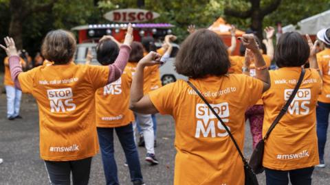 A group of people are wearing orange t-shirts that say Stop MS on them