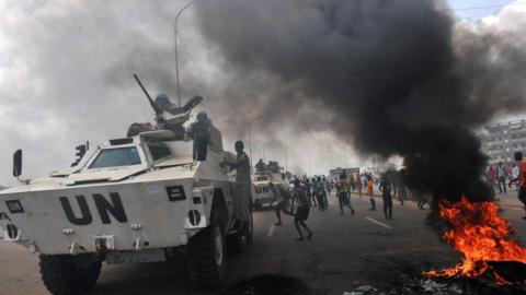 A UN tank rolls back by burning tires in a street in Ivory Coast