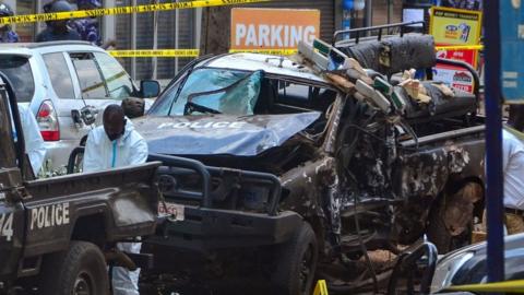 Police officers in Personal Protective Equipment (PPE) investigate around the police cars destroyed by a bomb explosion