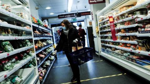 Woman in mask examines produce on shelves