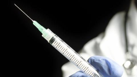 Stock image of a syringe being held in a blue-gloved hand