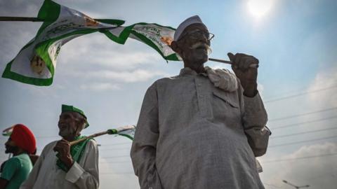 An elderly farmer holds a flag as he with others gather at the protest venue in Gazipur Delhi-Uttar Pradesh border during a nationwide strike called by the farmers as they continue to protest against the central government's agricultural reforms in Ghaziabad on September 27, 2021