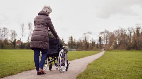 A woman pushing a man who is using a wheelchair