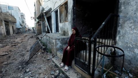 A Palestinian woman sits in front of a damaged building after the Israeli military's withdrawal from the Jenin refugee camp, in Jenin, in the occupied West Bank (5 July 2023)