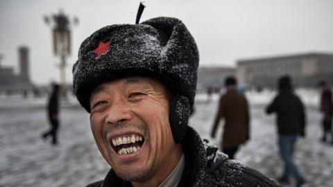 A Chinese vendor laughs as he stands in Tiananmen Square during a snowfall on November 22, 2014 in Beijing, China.