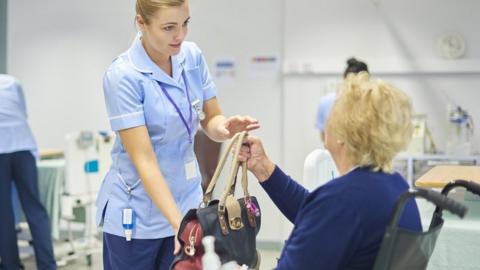 A patient is handed her bag by a nurse