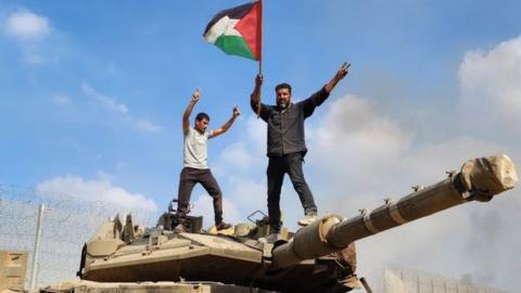 Gazans stand on top of a destroyed Israeli tank in Gaza