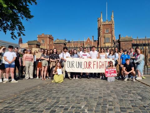 A group of students gathered outside Queen's University holding a signed reading 'our uni, our fight'