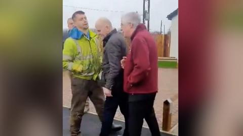 Protestor confronting Mark Drakeford with security man stood between them