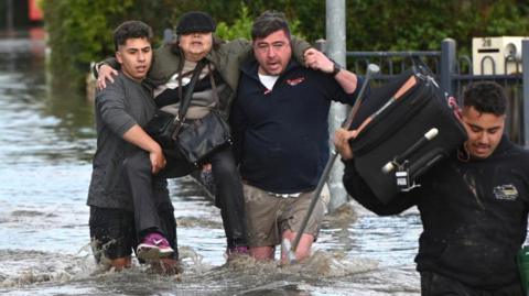 Two people carry a woman through floodwaters in Melbourne