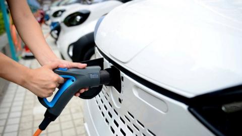 A staff member hooks up a charging cable to an electric vehicle