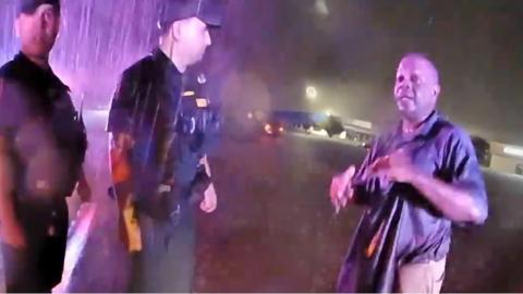 Two police officers and one man stand outside drenched in rain and flood water