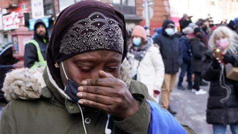 A woman cries as she walks past the 120-unit apartment building in the Bronx on 10 January, 2022, that was the site of a deadly fire yesterday in New York