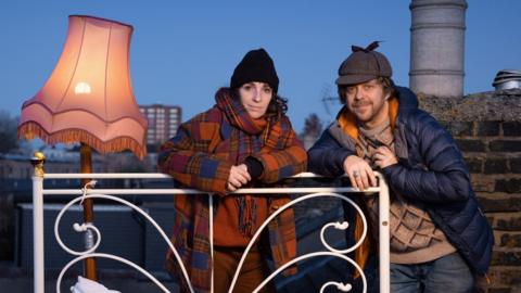 Dan and Hilary stand next to the bed on their roof