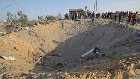 Palestinians gather around a crater after an Israeli air strike at Deir al-Balah, in Gaza