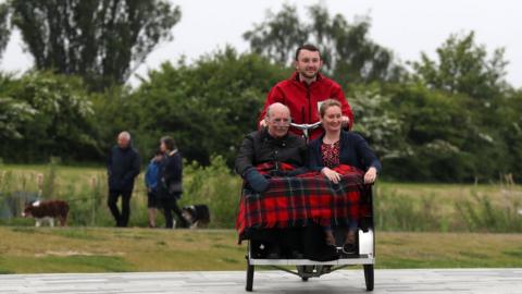 Lisa McCann and Lawrence Moffat are pedaled through the Helix Park as Public Health and Sport Minister Aileen Campbell helped to launch Cycling Without Age Scotland at the Kelpies in Falkirk