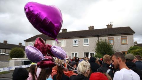 People hold pink heart-shaped balloons at the vigil for Chelsea and Christy Cawley and Lisa Cash outside their home in Tallaght in Dublin