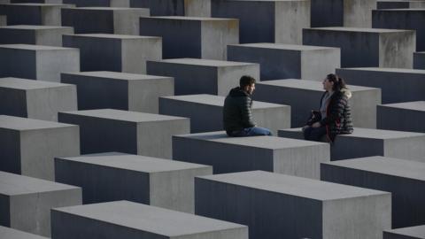 Visitors sit while visiting the Holocaust memorial in Berlin