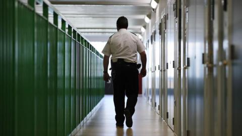 A prison guard walks a long a corridor