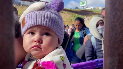 A migrant infant looks through the border wall