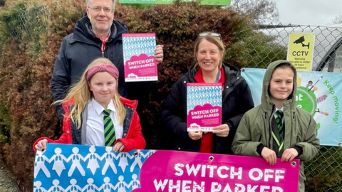 Paul West, eco council lead Mrs Daley and two pupils holding "switch off when parked" banner
