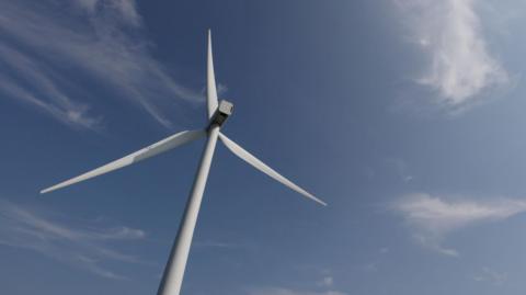 A view up to a white wind turbine against a blue sky with wispy white clouds.