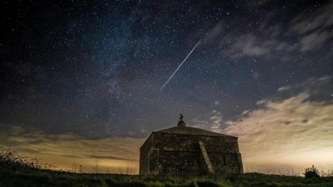 A meteor streaks in the night sky above a stone chapel in Dorset