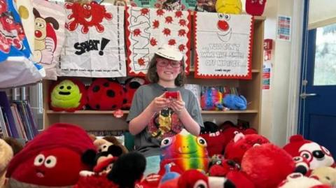 Ziggy surrounded by lots of red nose day merchandise, smiling