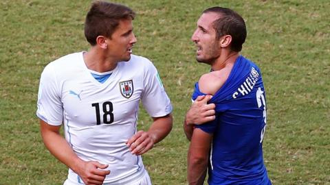 Giorgio Chiellini of Italy pulls down his shirt after a clash with Luis Suarez of Uruguay as Gaston Ramirez of Uruguay looks on during the 2014 FIFA World Cup Brazil Group D match between Italy and Uruguay at Estadio das Dunas