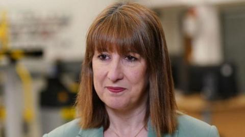 Rachel Reeves with a slight smile, dark red lipstick and shoulder length brown hair with a fringe. She is wearing a pale green top.