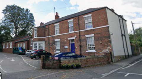 A screenshot from Google streetview of a brick school building with cars parked at the front. 