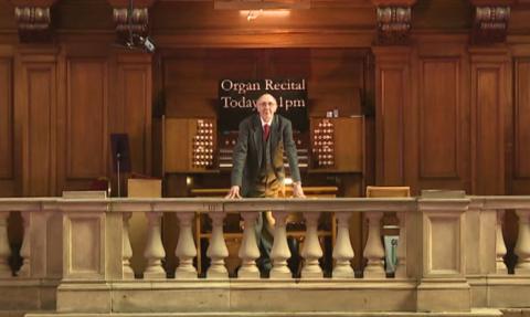 Organist stands on stone balcony in front of Kelvingrove organ.