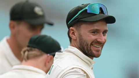 Joe Clarke is wearing his green Nottinghamshire cap with his sunglasses on top and is smiling at a team-mate 