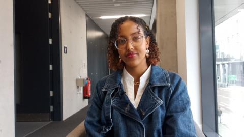 Esla Ibrahim, who has curly hair and wears a denim jacket stares at the camera 