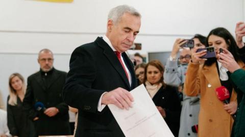 Calin Georgescu looks down as he casts his vote as a crowd looks on