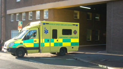 A States of Jersey Ambulance Service emergency ambulance driving out of the hospital building entrance in Jersey.