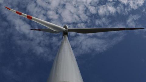 Close up image of a wind turbine set against a blue sky with white clouds