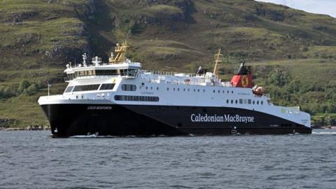 Loch Seaforth ferry. It is on the water with a hill behind it. The ferry is mainly white at the top with blue underneath. It has a red and black funnel and its name and Caledonian MacBrayne written in white on the side