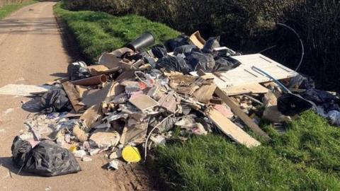 Bags of rubbish, wood and cardboard sprawled across the side of a road