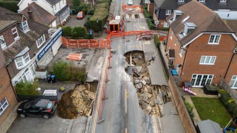 An aerial image of a sinkhole in a road, with houses to the left and right