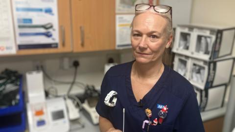 Amanda Beard holding a nasal swab which is used to detect flu. Behind her is a machine on a worktop which gives the result of the swab test within minutes