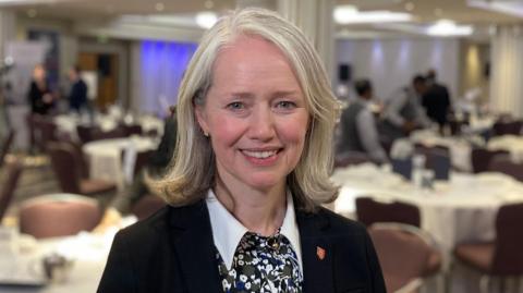 Deputy Kristina Moore is pictured in a hall with lots of tables behind her. 