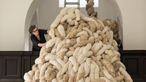 A woman arranges a huge woollen sculpture in an old building
