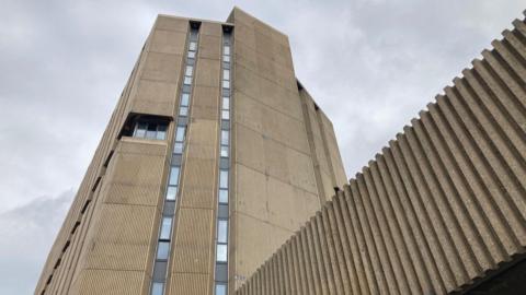 A brown-coloured concrete building with two lines of slitted windows running vertically upwards.