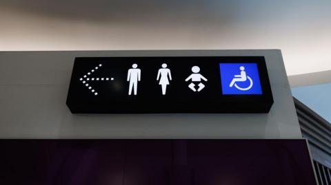 A photo shows a toilet sign with male, female, child and disabled icons