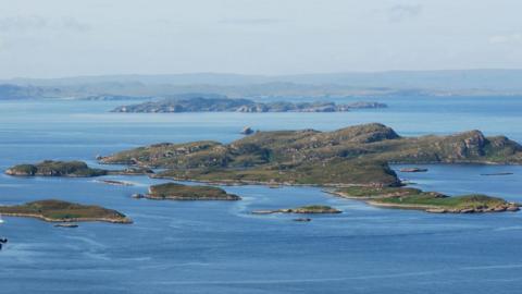 Small islands dot the loch. There is a white yacht anchored in a bay.