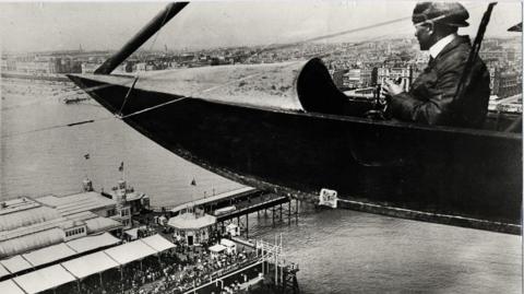 Black and white image of a seaplane flying over Brighton pier circa early 20th Century