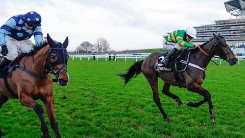 Jonbon and Thistle Ask clear the last fence and race towards the line. Jonbon's jockey, James Bowen, is wearing a white cap and a green-and-gold top. Thistle Ask is being ridden by Harry Skelton, who has a blue cap and top with lighter blue dots.