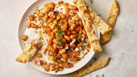 Browned beans sit on a plate of whipped feta accompanied by slices of pita bread